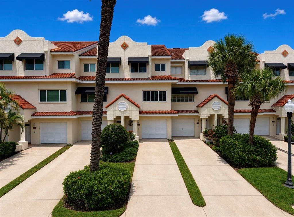 A row of multi-story townhomes with white stucco facades, red tile roofs, and attached garages — 4629 MIRABELLA COURT, ST PETE BEACH, FL