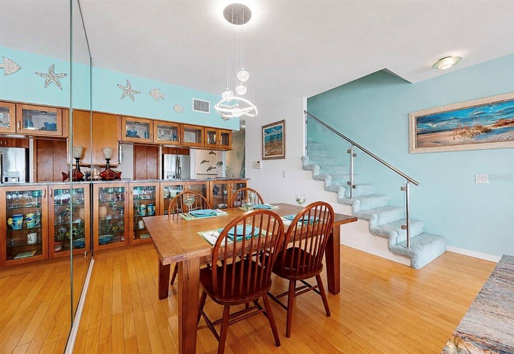 A dining room with a wooden table, chairs, glass-front cabinets, and stairs with glass railings — 4629 MIRABELLA COURT, ST PETE BEACH, FL
