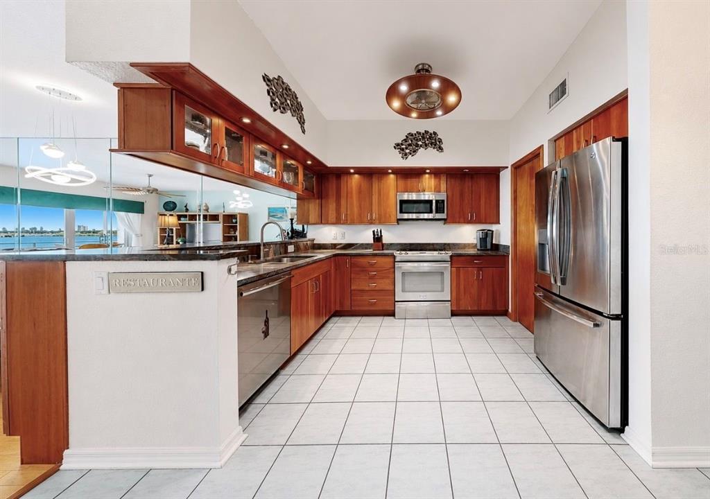A kitchen with wood cabinets, stainless steel appliances, and white tile flooring — 4629 MIRABELLA COURT, ST PETE BEACH, FL