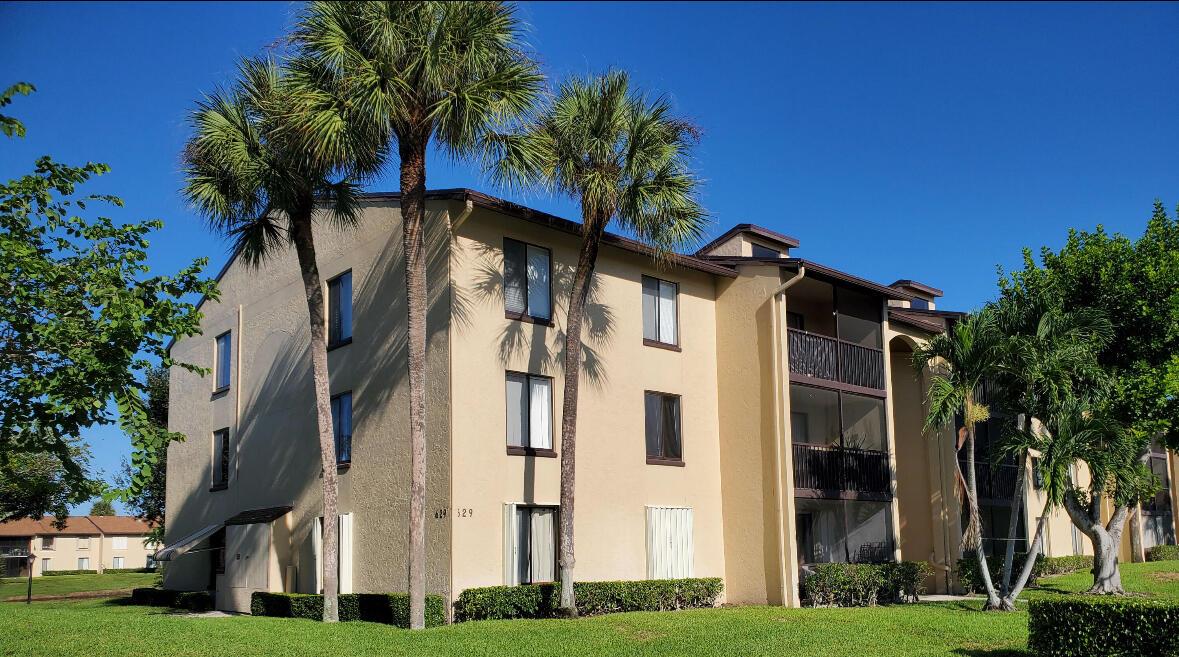 A three-story apartment building with beige stucco walls, screened balconies, and surrounding palm trees — 629 Sea Pine Way # A1, FL 33415, FL