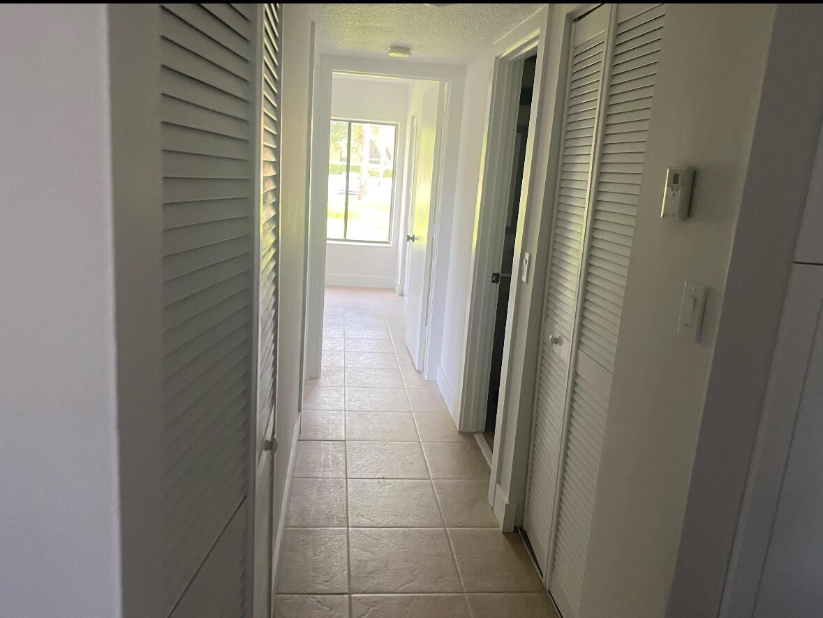 A narrow hallway with light-colored tile flooring and white louvered closet doors leads to a window — 629 Sea Pine Way # A1, FL 33415, FL