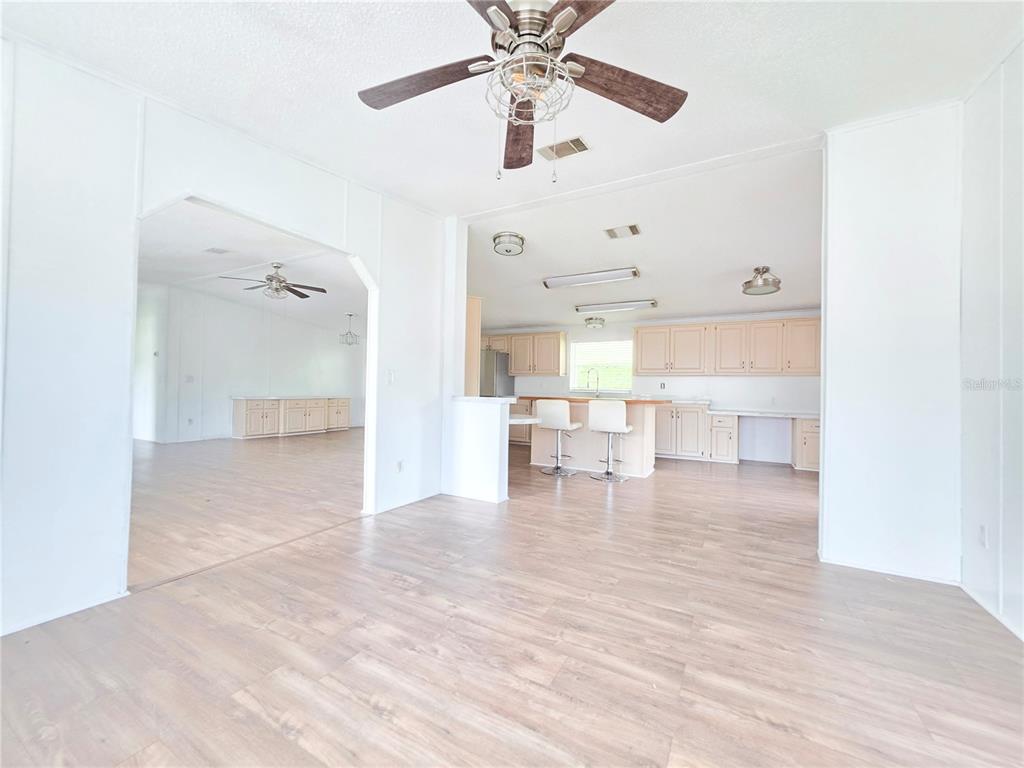 A bright, open-concept living area with light wood-look flooring, a ceiling fan, and kitchen — 1000 WALKER STREET UNIT 396, HOLLY HILL, FL