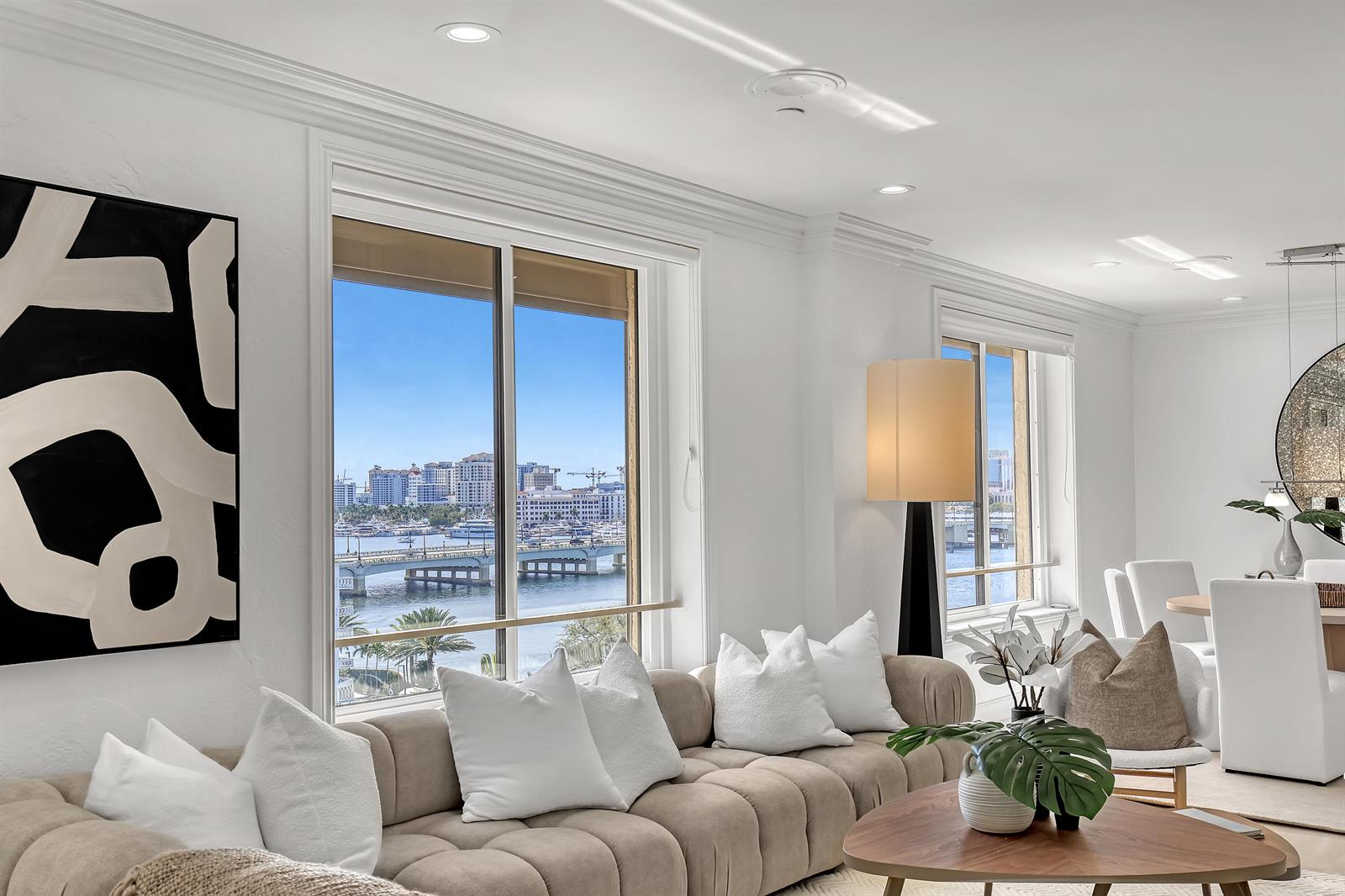 A modern living room features a tufted beige sofa, white decor, and a waterfront city view — 150 Bradley Place # 605, Palm Beach FL 33480, PALM BEACH, FL