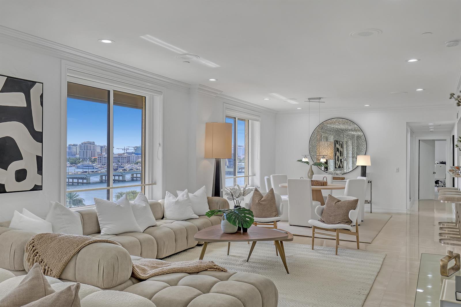 A bright, open-concept living and dining area features neutral furniture, a large round mirror, and waterfront views — 150 Bradley Place # 605, Palm Beach FL 33480, PALM BEACH, FL