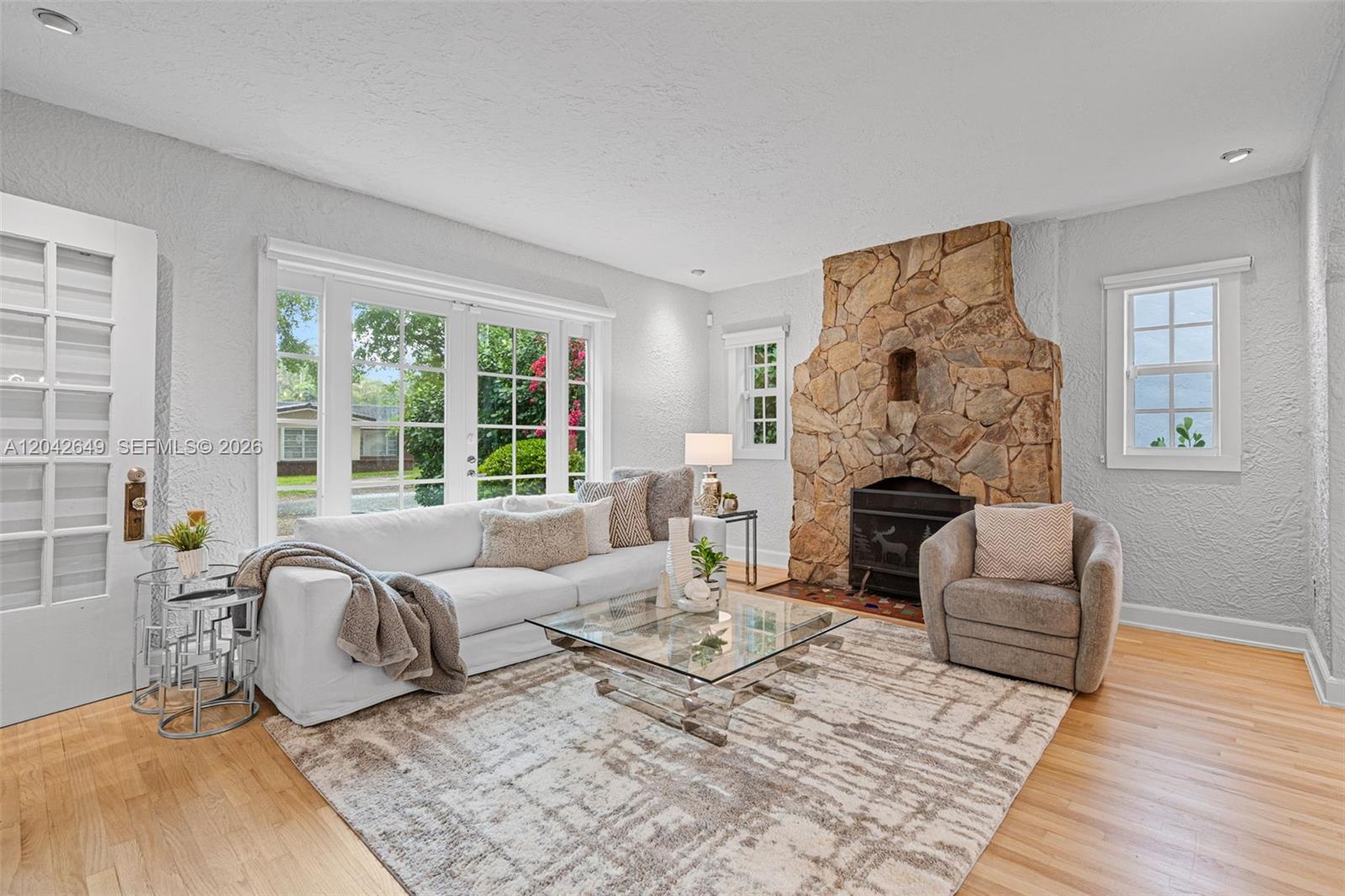 A living room features a stone fireplace, a white sofa, and glass coffee table — 1209 La Mancha Ave, Coral Gables FL 33134, CORAL GABLES, FL