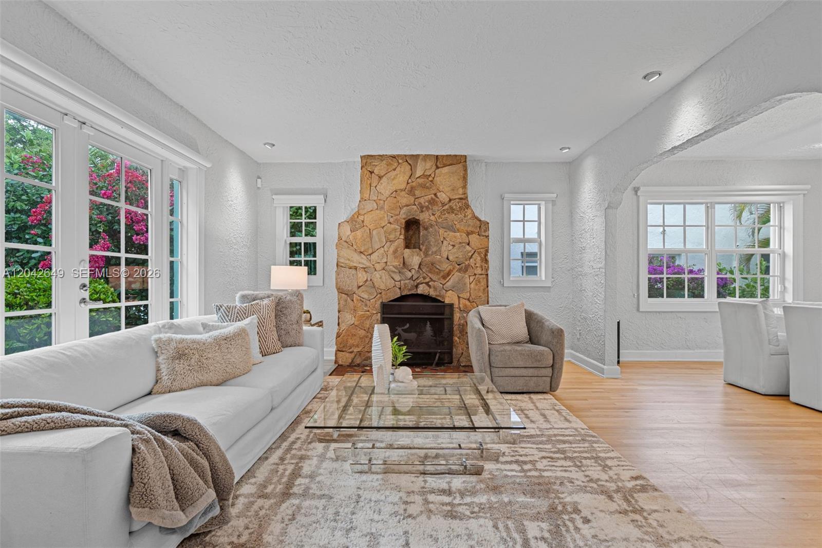 A living room features a stone fireplace, white walls, hardwood floors, and a glass coffee table — 1209 La Mancha Ave, Coral Gables FL 33134, CORAL GABLES, FL