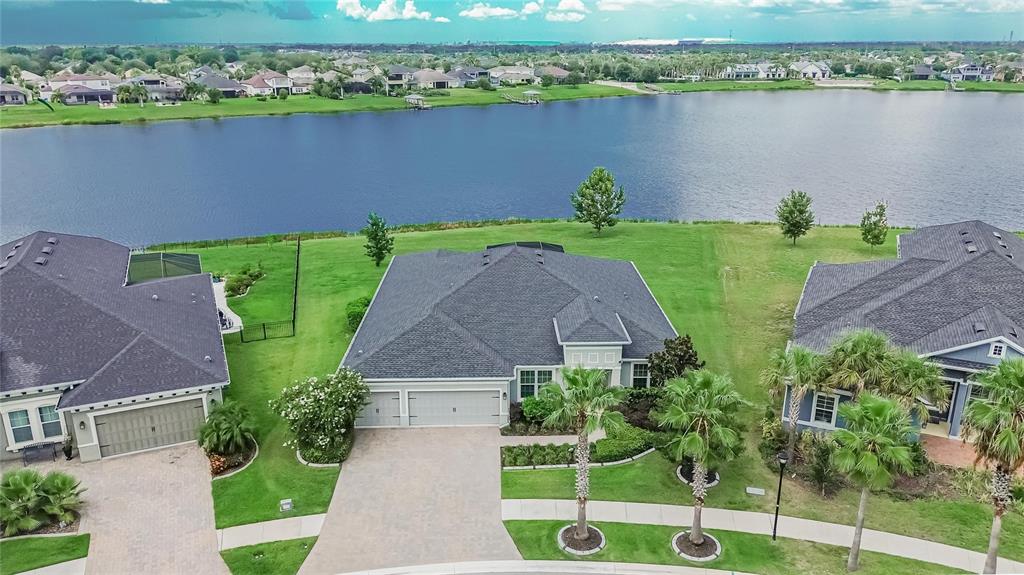 An aerial view shows three suburban houses with gray roofs and driveways facing a large lake — 12313 NORA GRANT PLACE, RIVERVIEW, FL