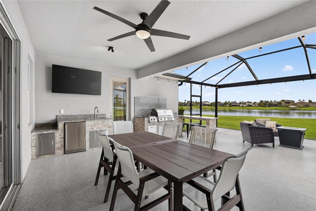 A covered outdoor patio features a dining table, a built-in kitchen, and a screened-in pool area — 12313 NORA GRANT PLACE, RIVERVIEW, FL