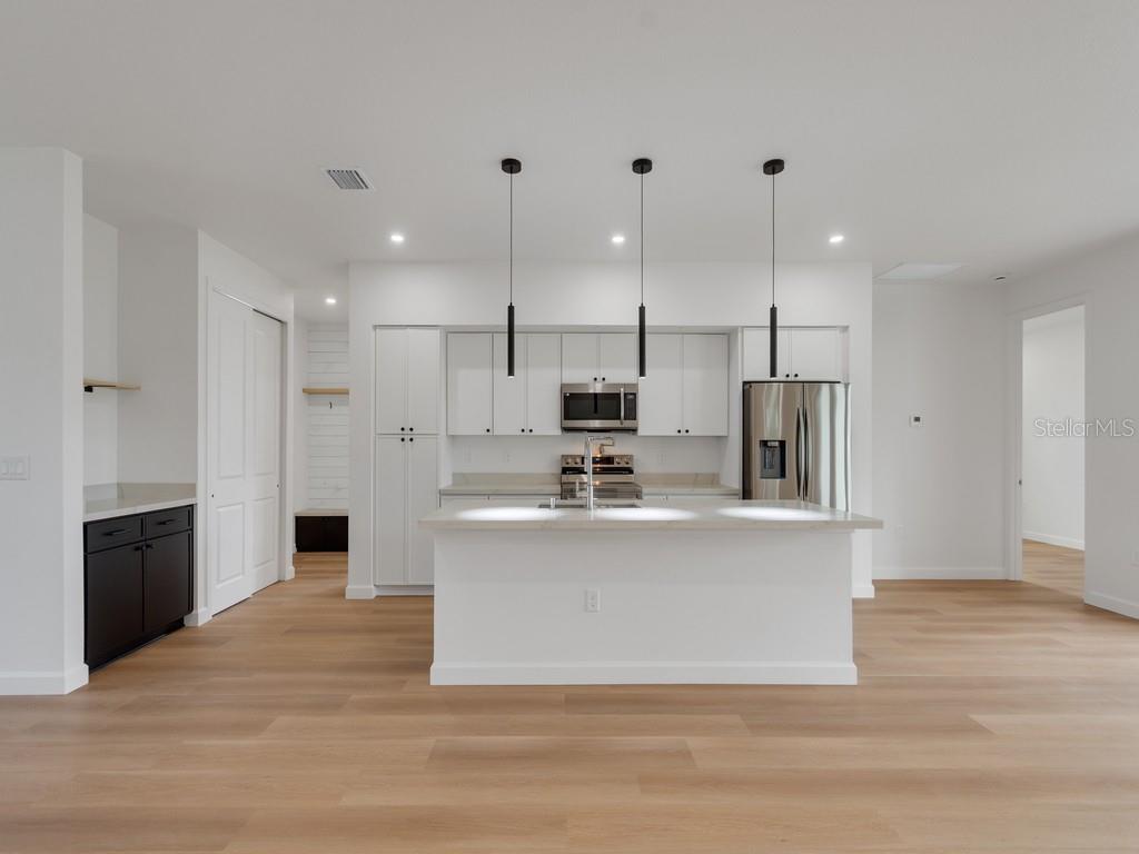 A modern kitchen features white cabinetry, a central island, stainless steel appliances, and light flooring — 2602 DE GROODT ROAD SW, PALM BAY, FL