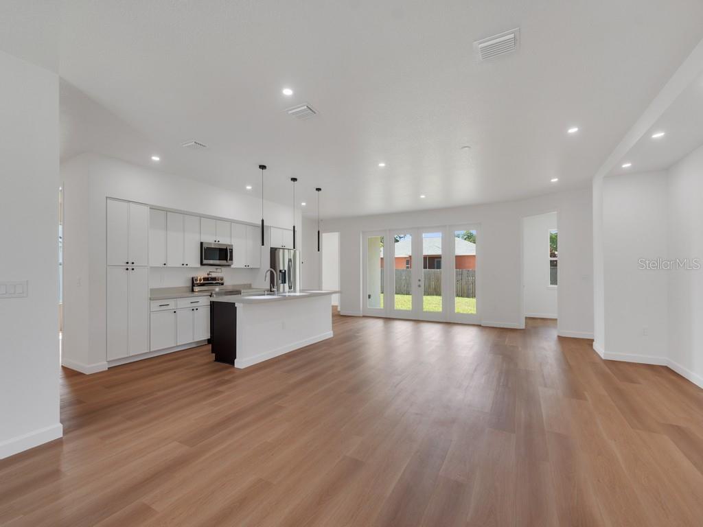 A modern open-concept kitchen and living area features white cabinetry, a kitchen island, and flooring — 2602 DE GROODT ROAD SW, PALM BAY, FL