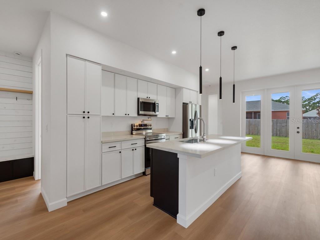 A modern kitchen features white cabinetry, a dark island with a sink, and light wood flooring — 2602 DE GROODT ROAD SW, PALM BAY, FL