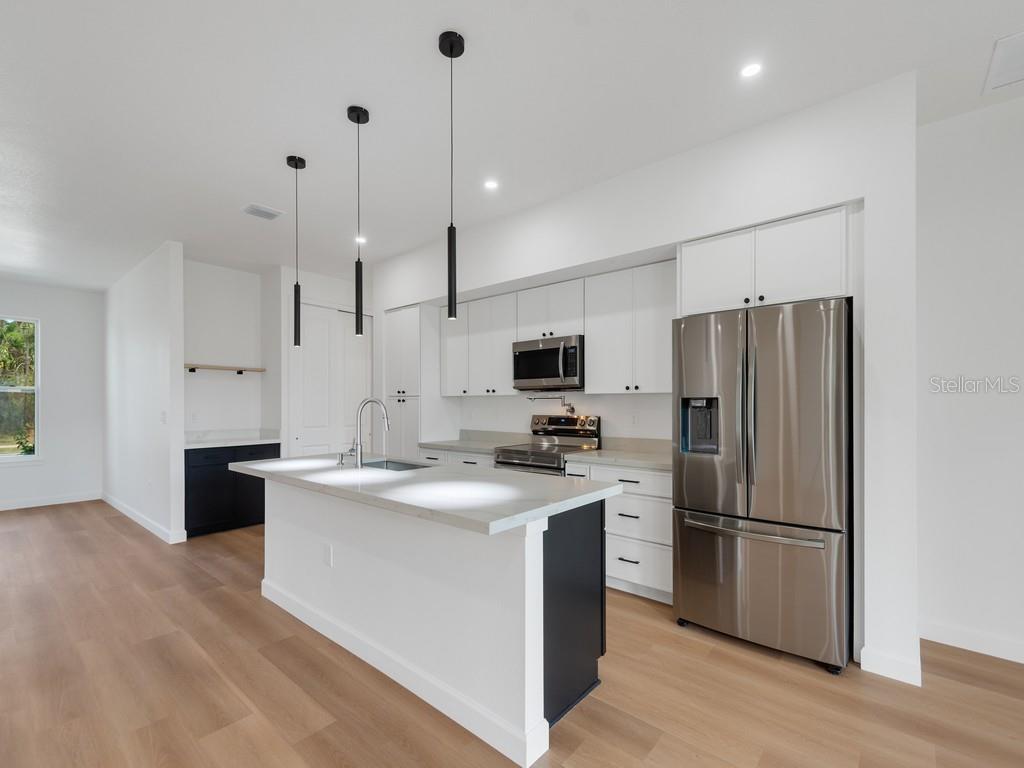 A modern kitchen features white cabinetry, a central island, stainless steel appliances, and wood flooring — 2602 DE GROODT ROAD SW, PALM BAY, FL