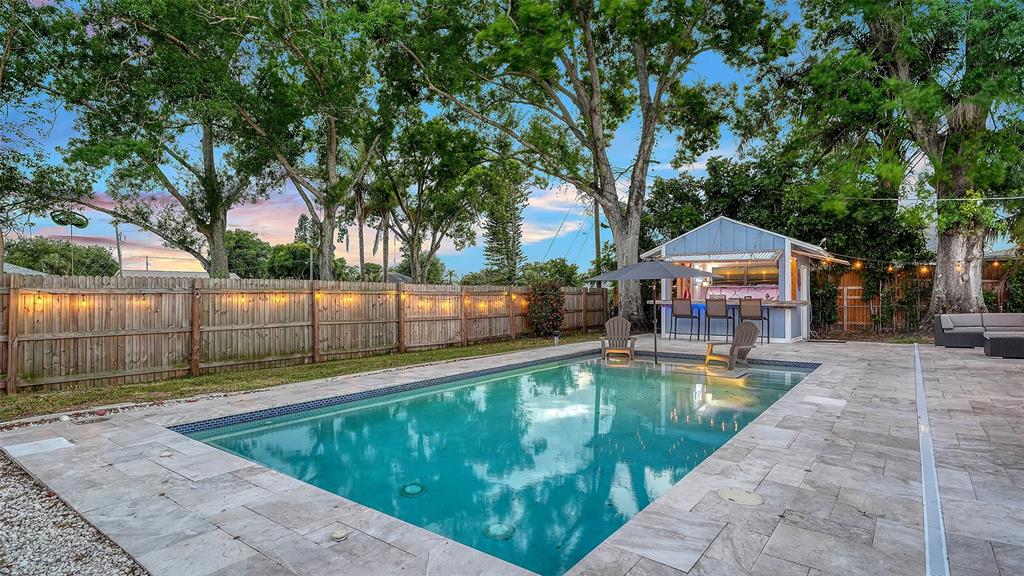 A backyard features a rectangular swimming pool, stone patio, wooden fence, and a small bar structure — 311 44TH STREET COURT W, PALMETTO, FL