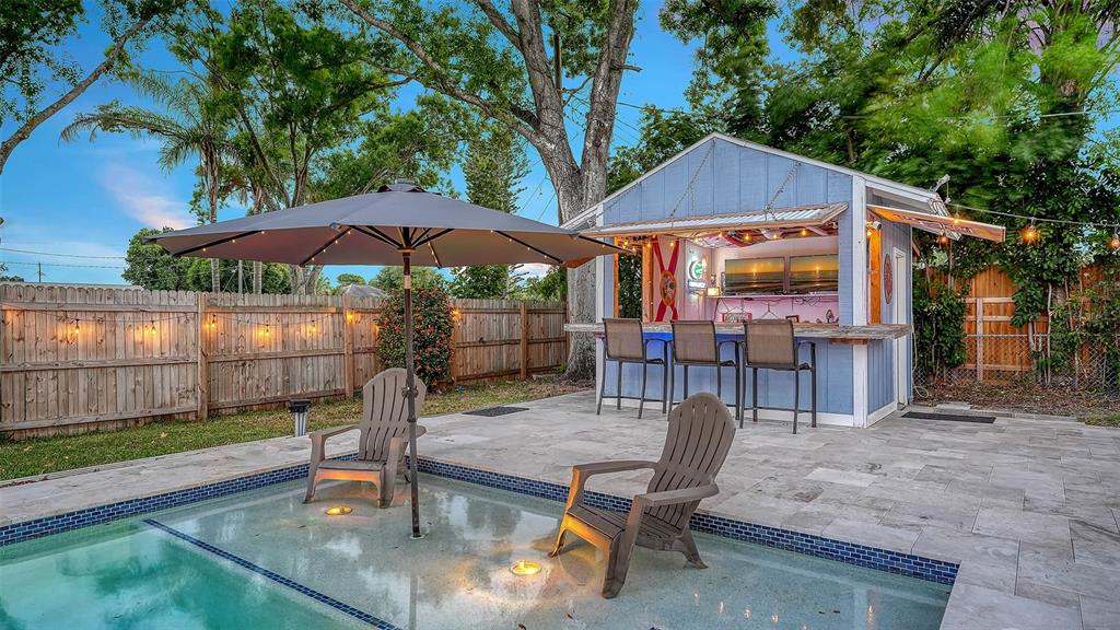 A backyard patio features a swimming pool, two chairs, a large umbrella, and a tiki bar — 311 44TH STREET COURT W, PALMETTO, FL