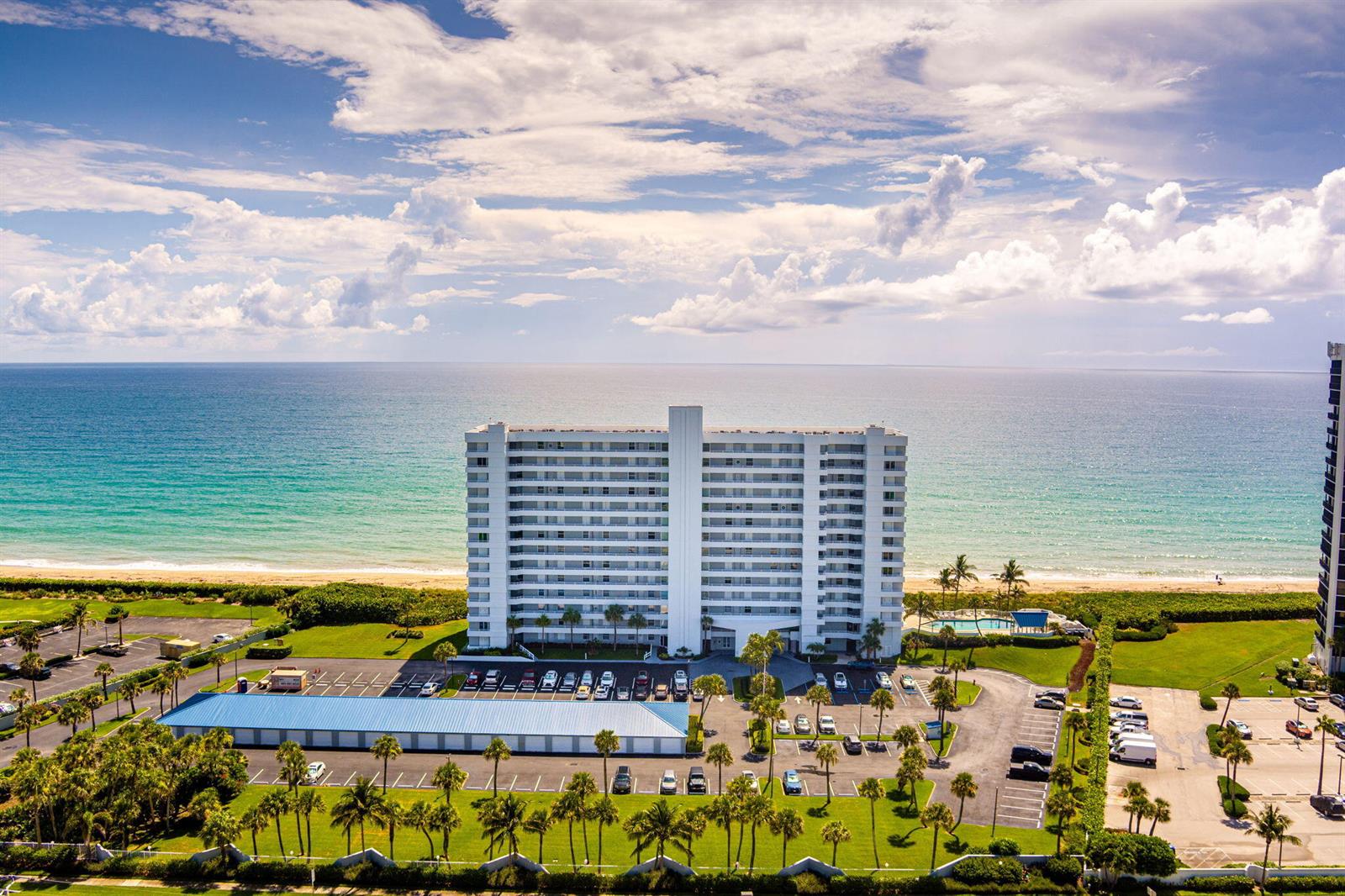 An aerial view shows a tall beachfront condominium building with a parking lot and pool — 9600 S Ocean Drive # 906, Jensen Beach FL 34957, JENSEN BEACH, FL
