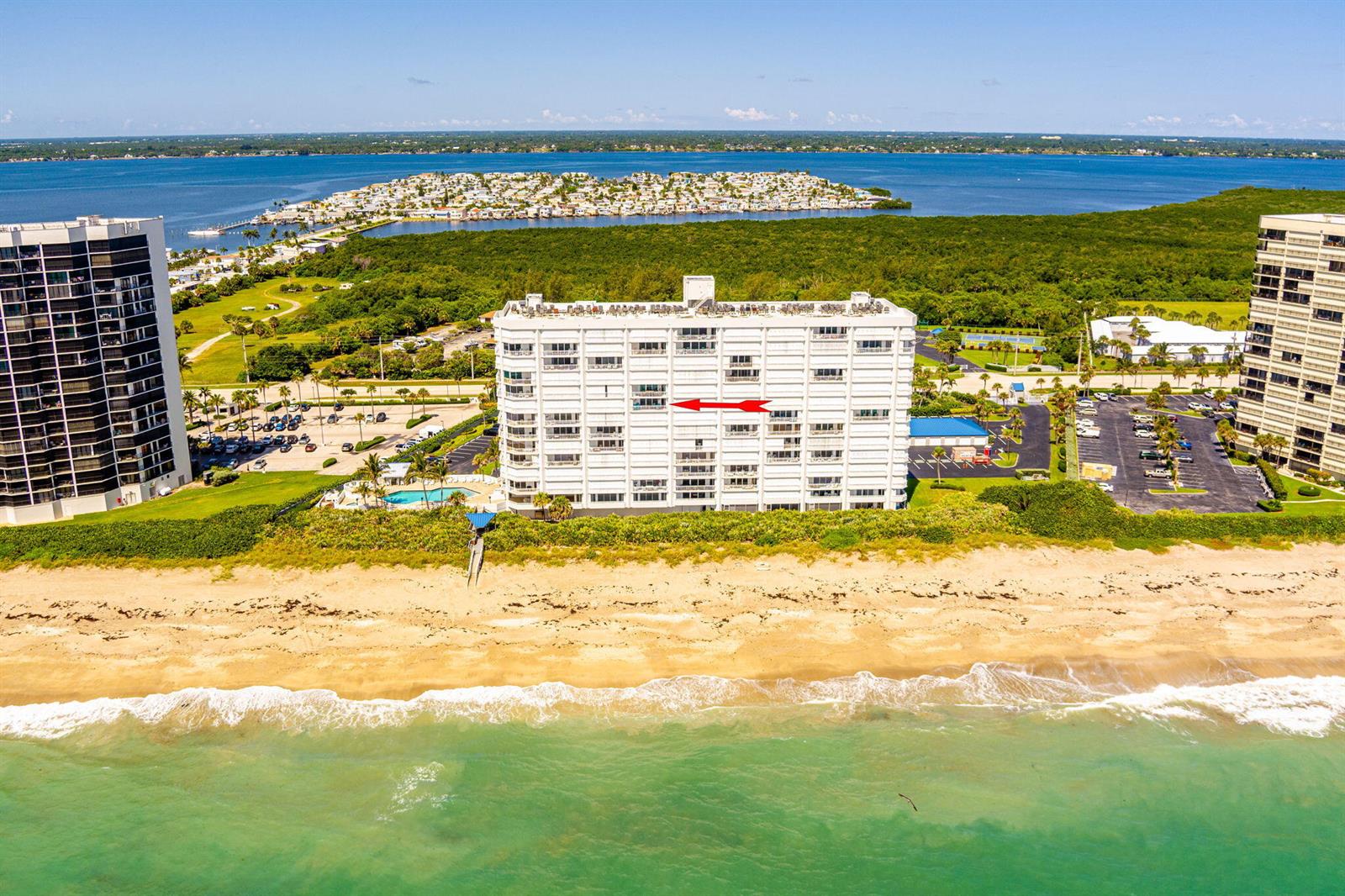 An aerial view shows a white beachfront condominium building with a red arrow pointing toward it — 9600 S Ocean Drive # 906, Jensen Beach FL 34957, JENSEN BEACH, FL