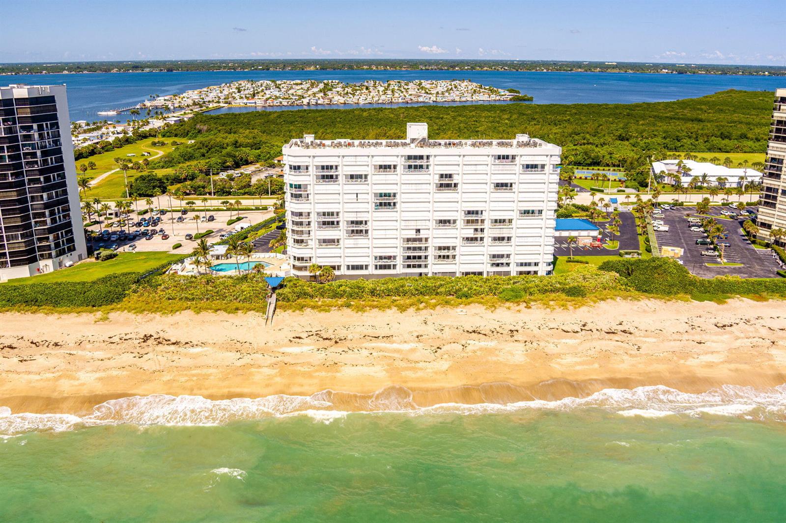 An aerial view shows a white multi-story apartment building situated directly on a sandy beach — 9600 S Ocean Drive # 906, Jensen Beach FL 34957, JENSEN BEACH, FL