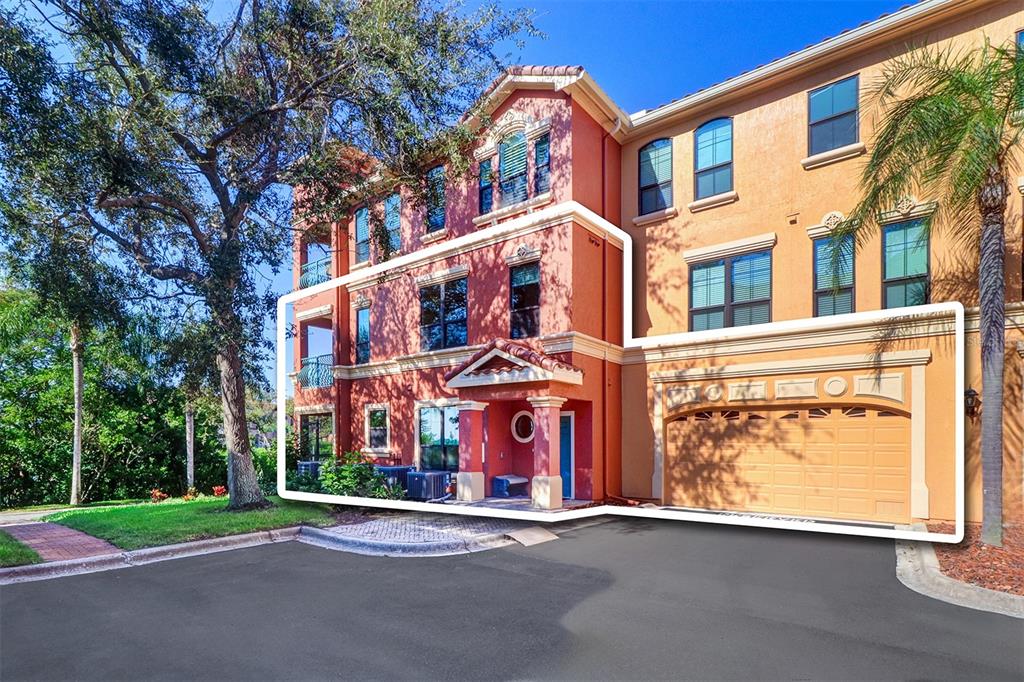 A three-story townhouse exterior with a red facade, a front entrance, and an attached garage — 2757 VIA CIPRIANI UNIT 1114A, CLEARWATER, FL