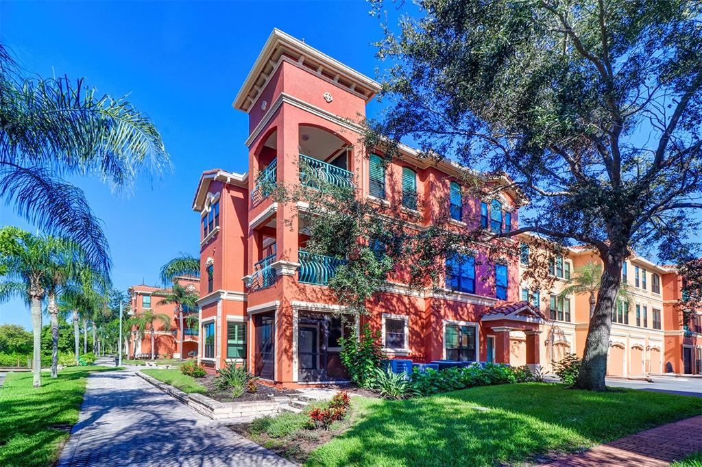A three-story orange apartment building with balconies and a paved walkway under a blue sky — 2757 VIA CIPRIANI UNIT 1114A, CLEARWATER, FL
