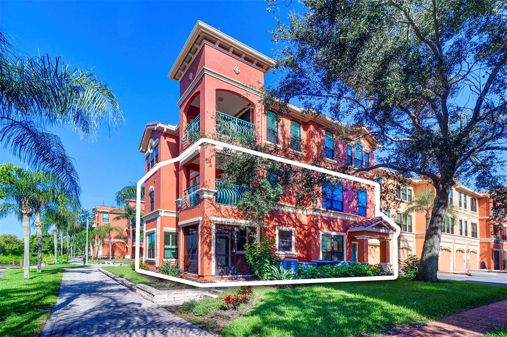 A three-story orange stucco apartment building features balconies, a screened-in patio, and lush landscaping — 2757 VIA CIPRIANI UNIT 1114A, CLEARWATER, FL