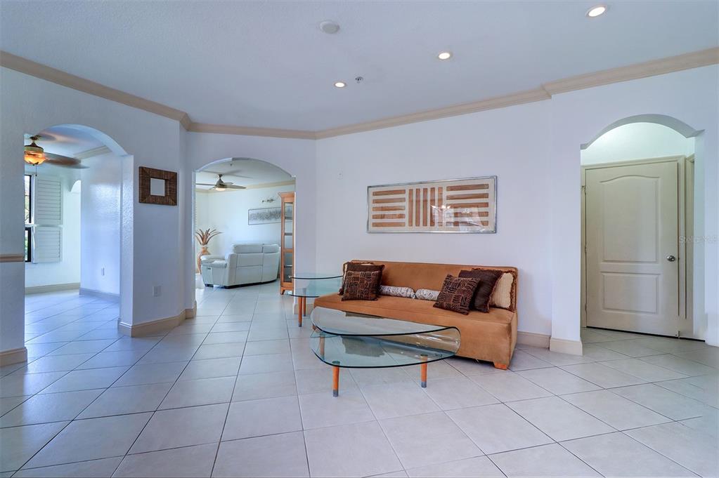 A living room features light tile floors, a tan sofa, and arched doorways — 2757 VIA CIPRIANI UNIT 1114A, CLEARWATER, FL