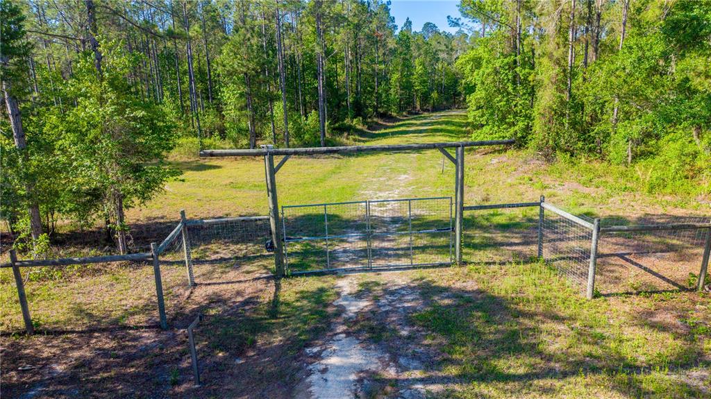 A metal gate stands at the entrance of a dirt path leading into a wooded area — TBD NW 57TH LANE, STARKE, FL