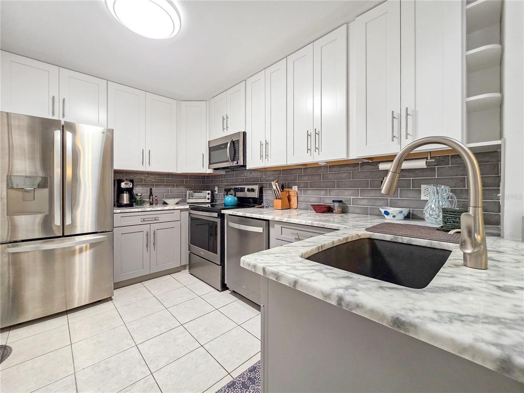 A kitchen with white upper cabinets, gray lower cabinets, stainless steel appliances, and marble countertops — 3300 LOVELAND BOULEVARD UNIT 2904, PORT CHARLOTTE, FL