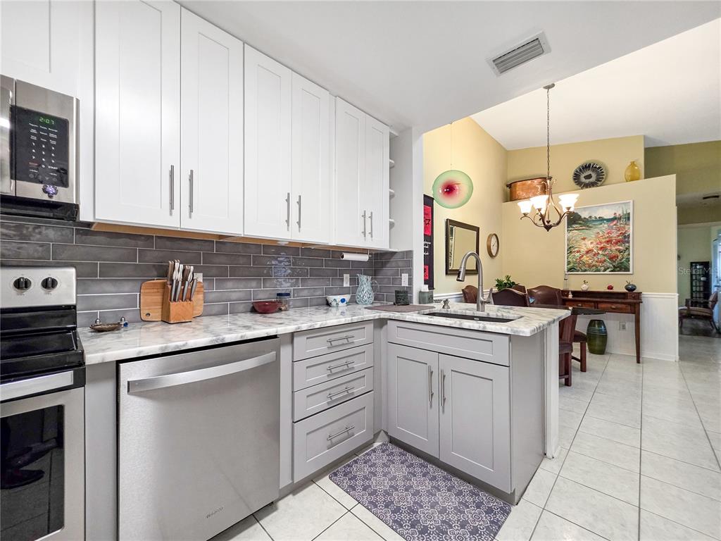 A kitchen features white upper cabinets, grey lower cabinets, stainless steel appliances, and tile flooring — 3300 LOVELAND BOULEVARD UNIT 2904, PORT CHARLOTTE, FL
