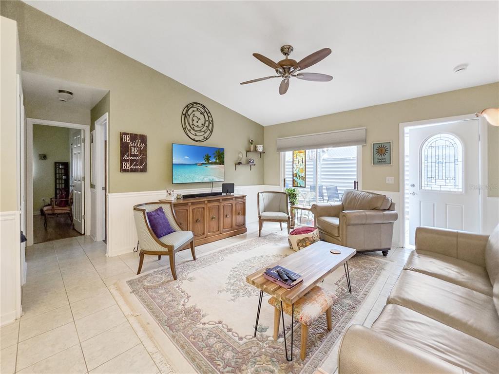 A living room features a vaulted ceiling, tile flooring, a television, and a ceiling fan — 3300 LOVELAND BOULEVARD UNIT 2904, PORT CHARLOTTE, FL