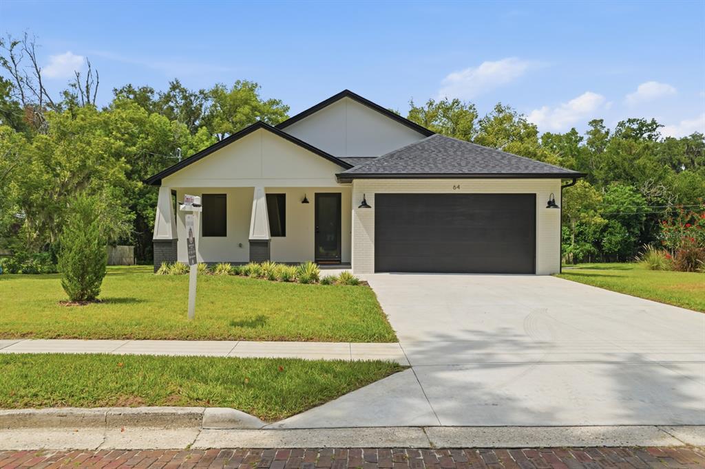 A modern single-story house with a white exterior, black garage door, and a front porch — 64 HIGHLAND STREET, BROOKSVILLE, FL