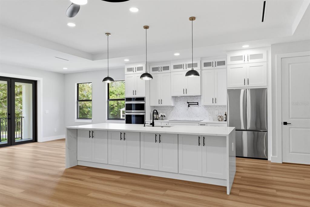 A modern white kitchen features a large island, stainless steel appliances, and light wood flooring — 64 HIGHLAND STREET, BROOKSVILLE, FL