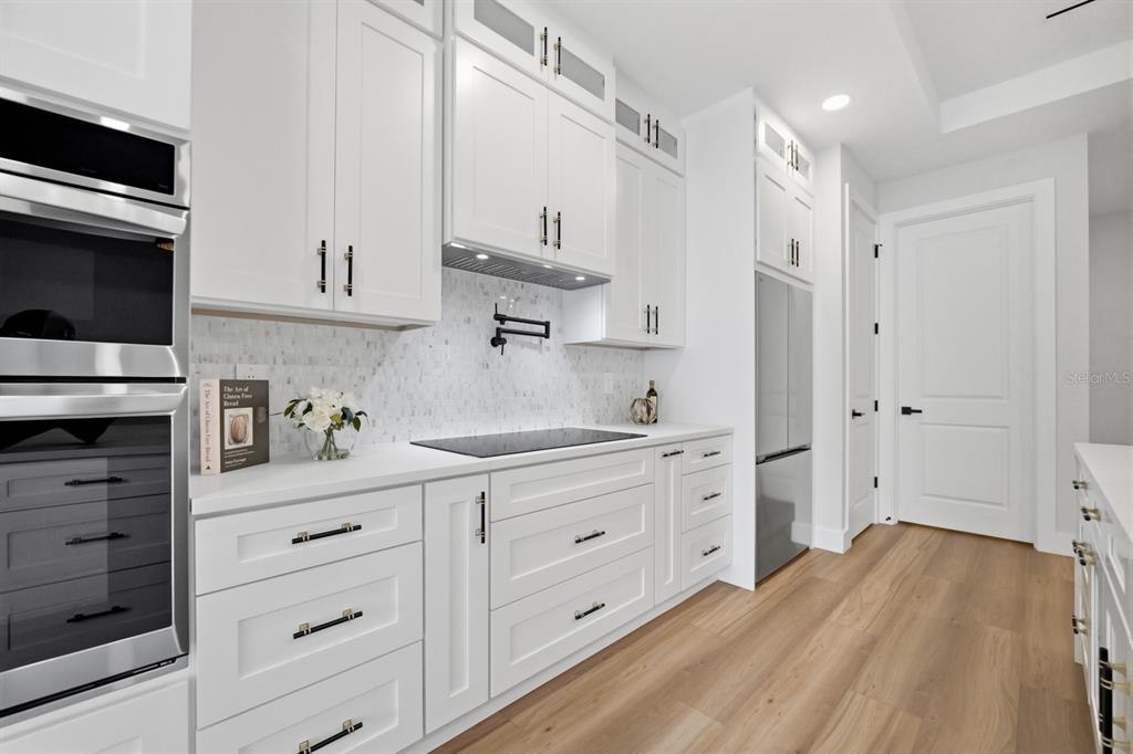 A modern white kitchen features stainless steel appliances, light wood flooring, and a tiled backsplash — 64 HIGHLAND STREET, BROOKSVILLE, FL