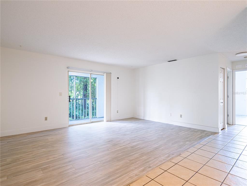 An empty living room features light wood-look flooring, white walls, and a sliding glass door — 101 BENT TREE DRIVE UNIT 75, DAYTONA BEACH, FL
