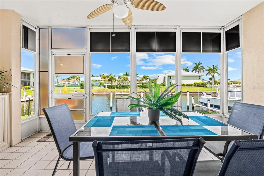 A sunroom features a glass-top dining table, tile flooring, and a view of a canal — 3640 BAL HARBOR BOULEVARD UNIT 112, PUNTA GORDA, FL