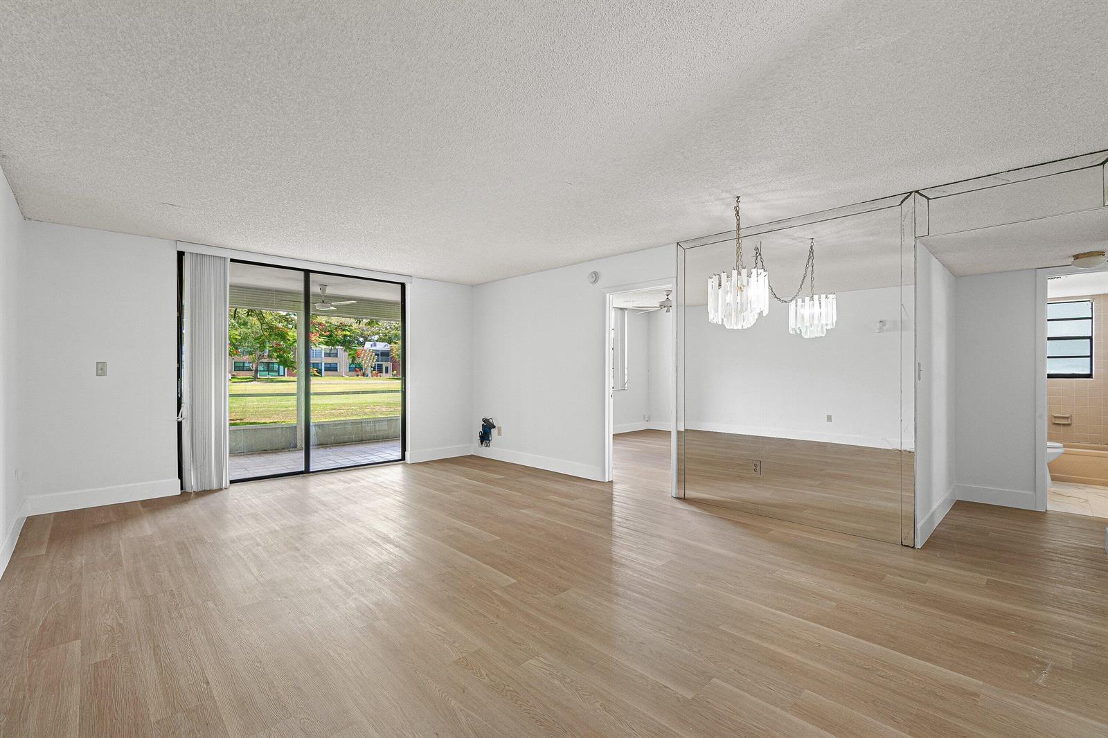 An empty living room with light wood-look flooring, a mirrored wall, and a sliding glass door — 7380 NW 18th Street # 108, Margate FL 33063, MARGATE, FL