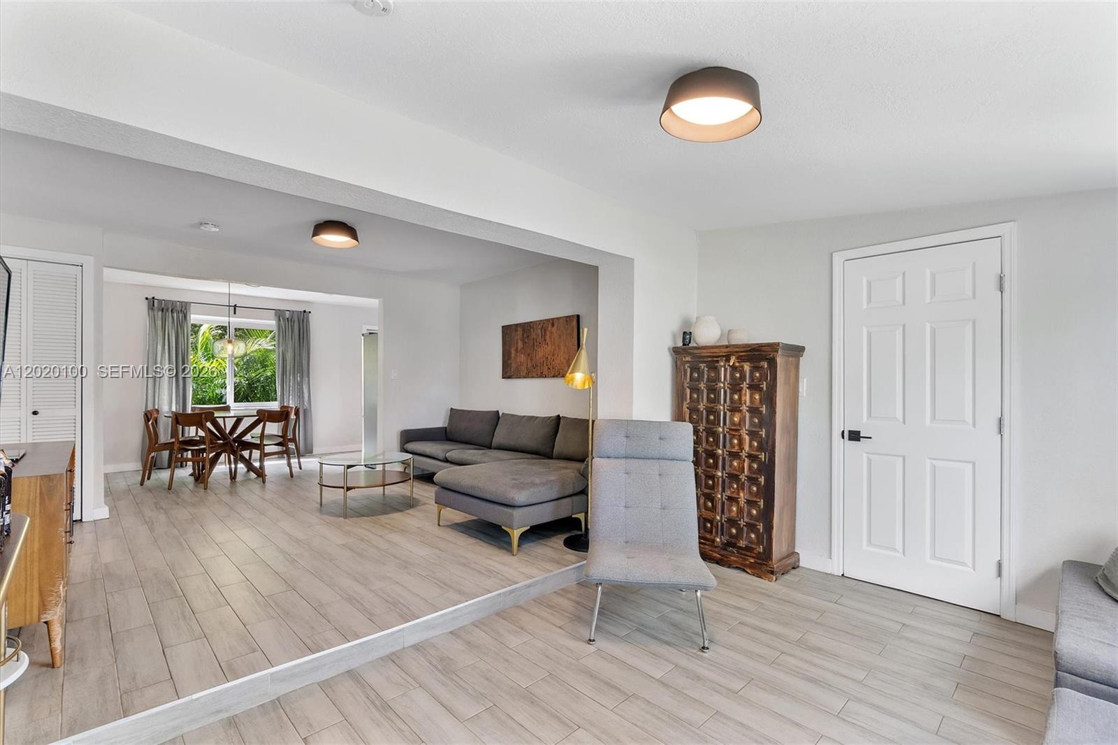 This living and dining area features light wood-look tile flooring, a sunken floor level, and gray furniture — 74 NW 117th St, Miami FL 33168, MIAMI, FL