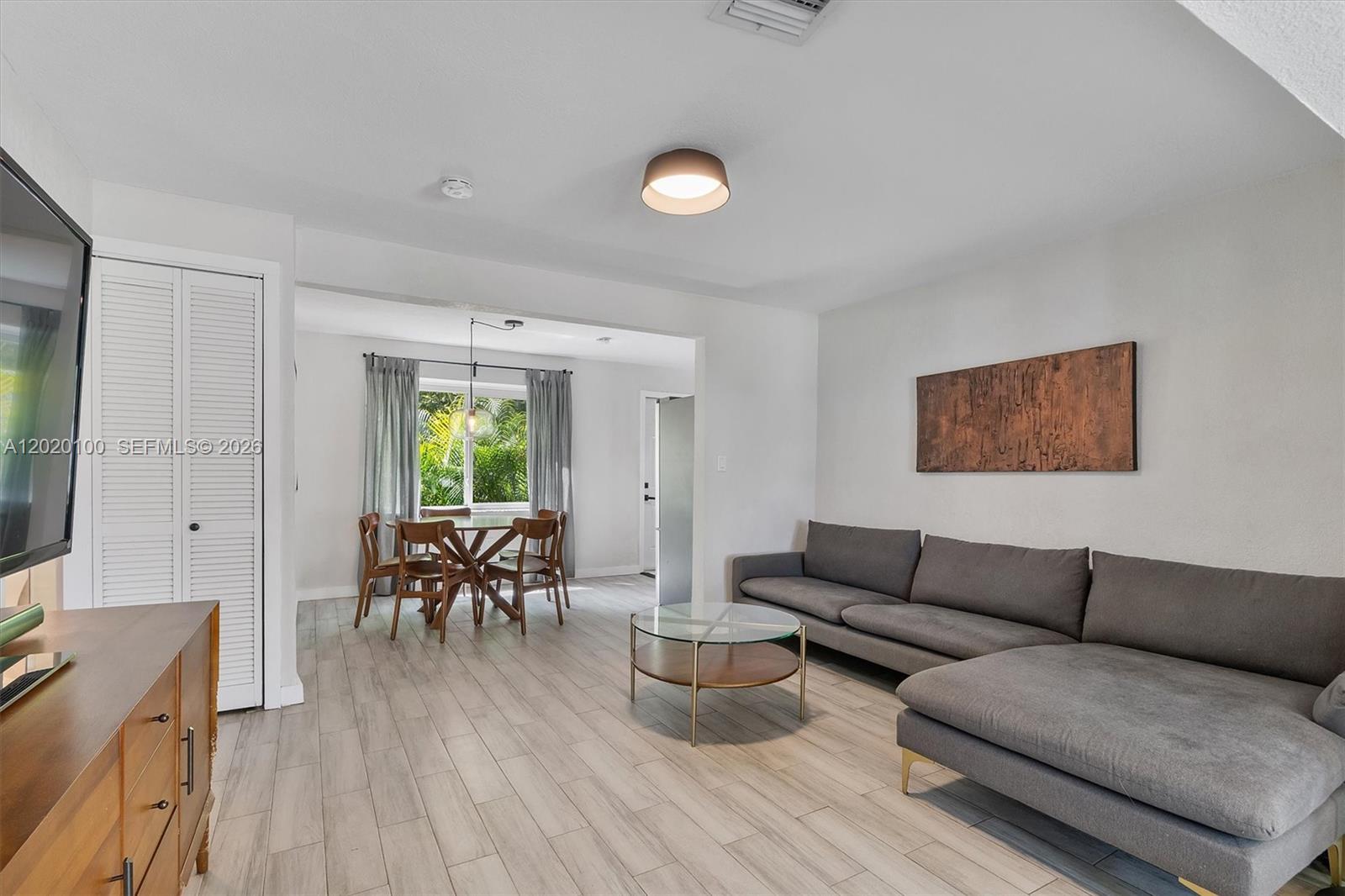 A living room and dining area feature gray tile flooring, a sectional sofa, and furniture — 74 NW 117th St, Miami FL 33168, MIAMI, FL