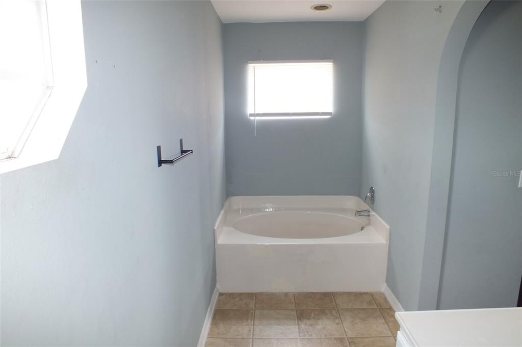 A bathroom features a built-in soaking tub, light blue walls, and beige floor tiles — 437 FISH HAWK DRIVE, WINTER HAVEN, FL