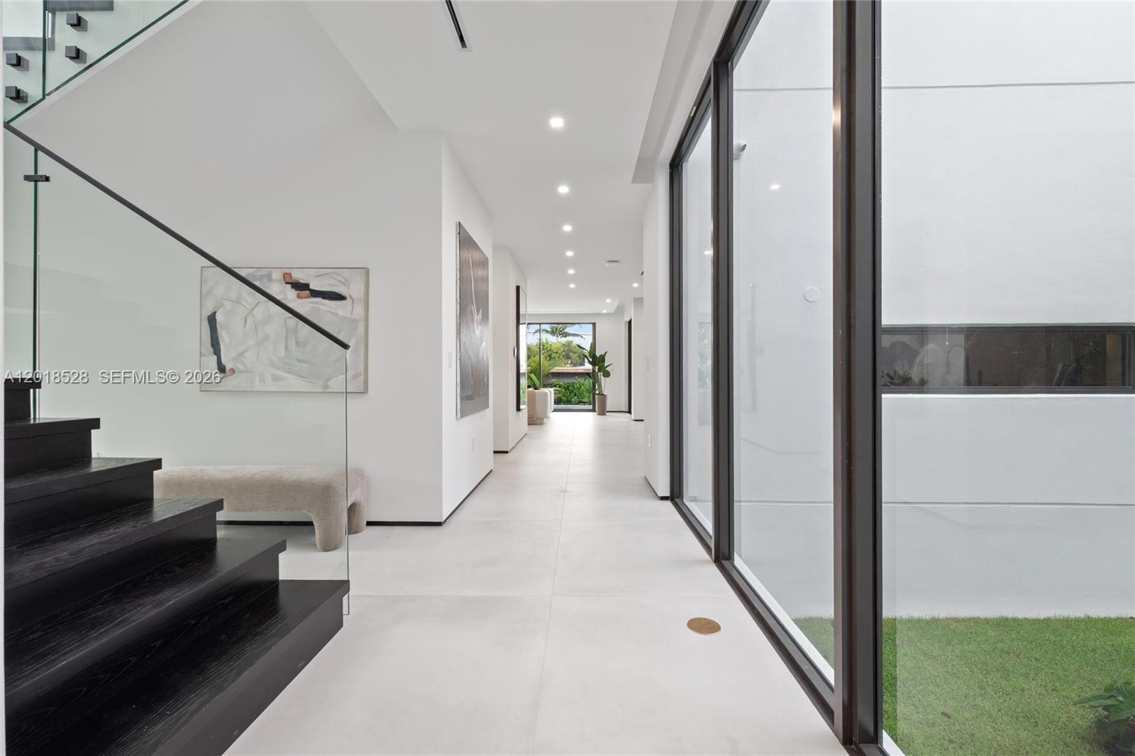 A modern hallway features white tile floors, black stairs, and floor-to-ceiling glass walls — 2096 Alamanda Dr, North Miami FL 33181, NORTH MIAMI, FL