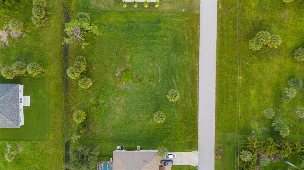 An aerial view shows a vacant, grassy residential lot situated between two houses and a road — 70 TEE VIEW ROAD, ROTONDA WEST, FL