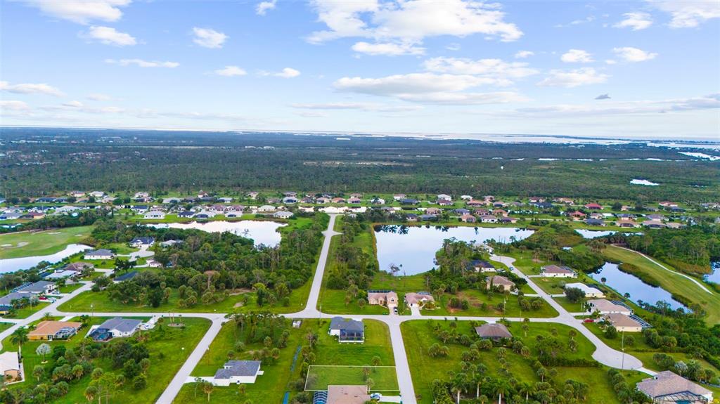 An aerial view shows a residential neighborhood with houses, ponds, and undeveloped lots — 70 TEE VIEW ROAD, ROTONDA WEST, FL