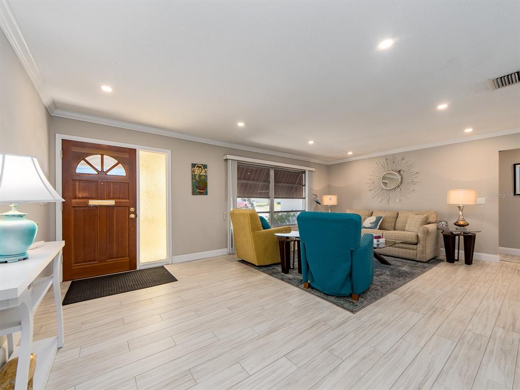 A living room features light wood-look tile flooring, a front door, and colorful armchairs — 9234 141ST STREET, SEMINOLE, FL