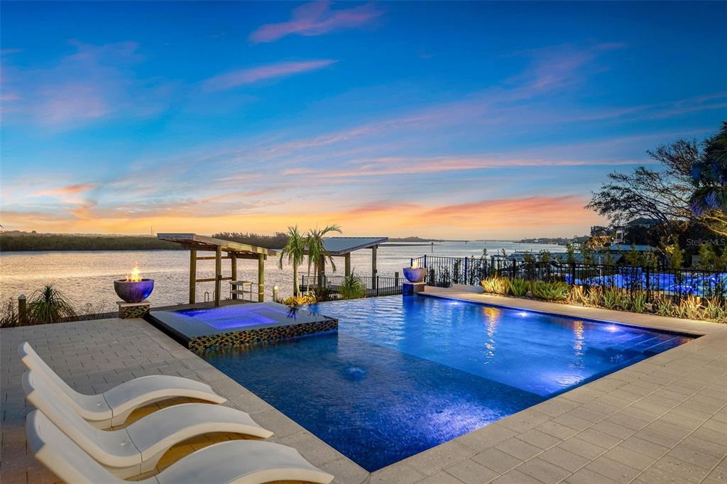 An infinity-edge pool and spa overlook a river at sunset with lounge chairs in foreground — 1194 N PENINSULA AVENUE, NEW SMYRNA BEACH, FL