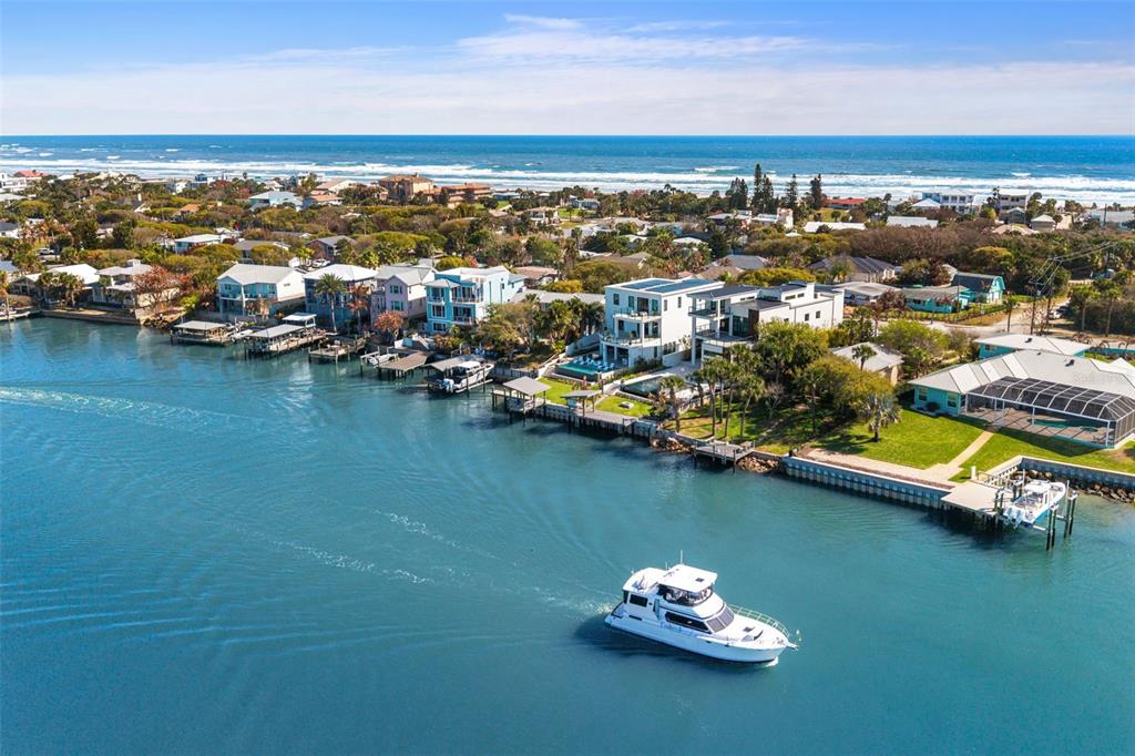 An aerial view shows a white boat traveling on a canal near coastal homes — 1194 N PENINSULA AVENUE, NEW SMYRNA BEACH, FL