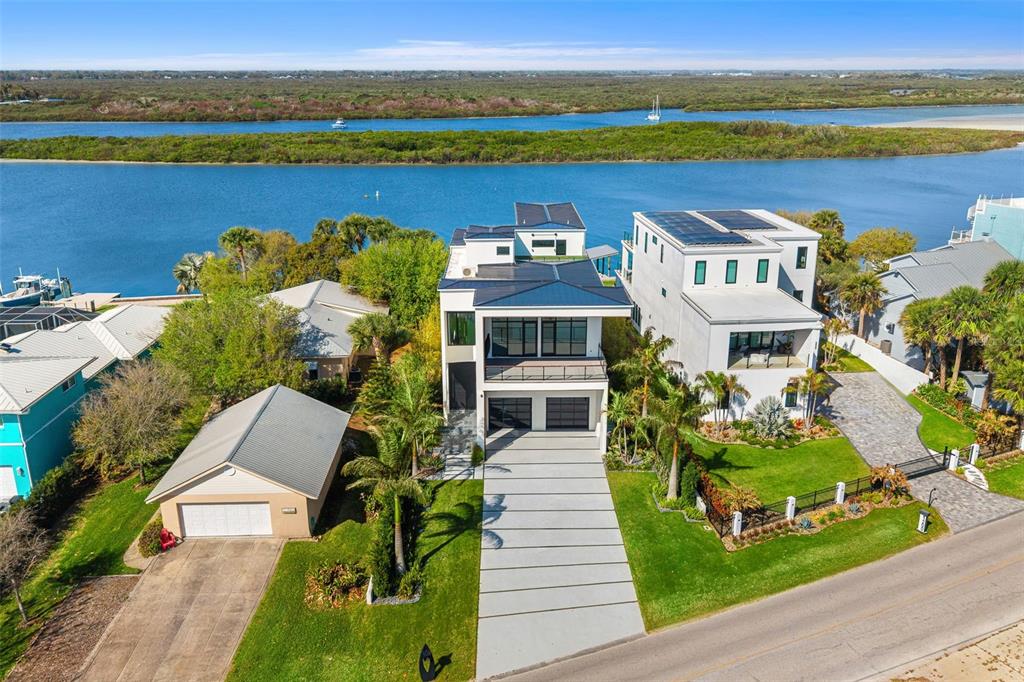 An aerial view shows three waterfront houses with modern architecture and solar panels on roofs — 1194 N PENINSULA AVENUE, NEW SMYRNA BEACH, FL