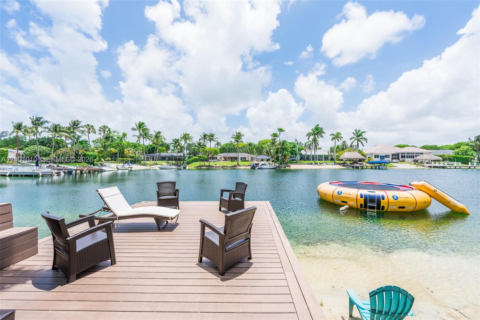 A wooden deck with outdoor furniture overlooks a canal with a floating water trampoline — 9240 SW 140th St, Miami FL 33176, MIAMI, FL