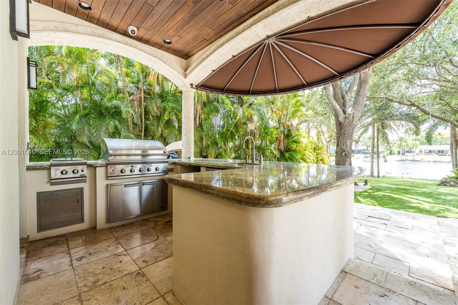 An outdoor kitchen features a granite countertop, stainless steel grill, and sink under a patio — 9240 SW 140th St, Miami FL 33176, MIAMI, FL