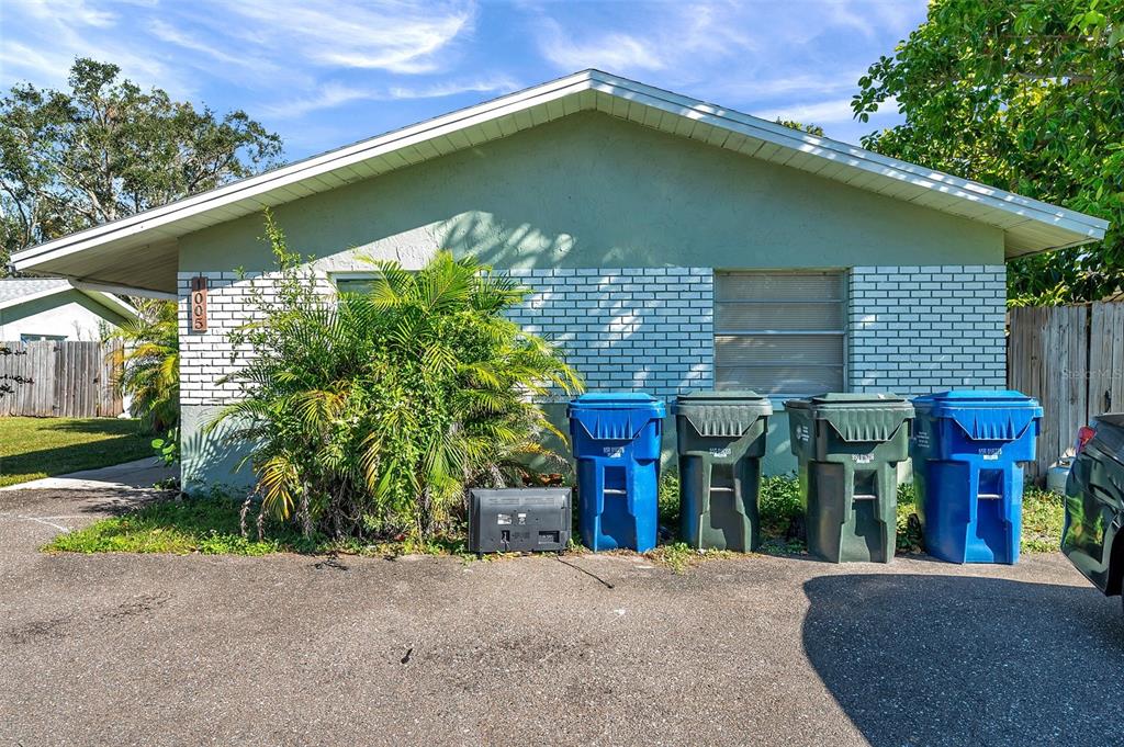 The exterior of a single-story house features a light green facade, brick accents, and four trash bins — 1005 LAKE PALMS DRIVE, LARGO, FL