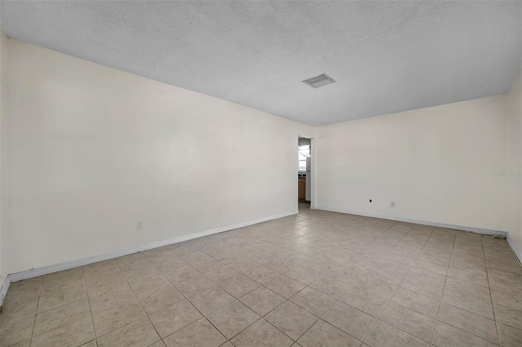 An empty room with beige tile flooring, white walls, and a doorway leading to a kitchen — 1005 LAKE PALMS DRIVE, LARGO, FL