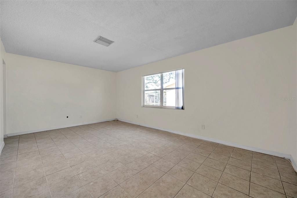 An empty room with beige tile flooring, off-white walls, and a single window — 1005 LAKE PALMS DRIVE, LARGO, FL